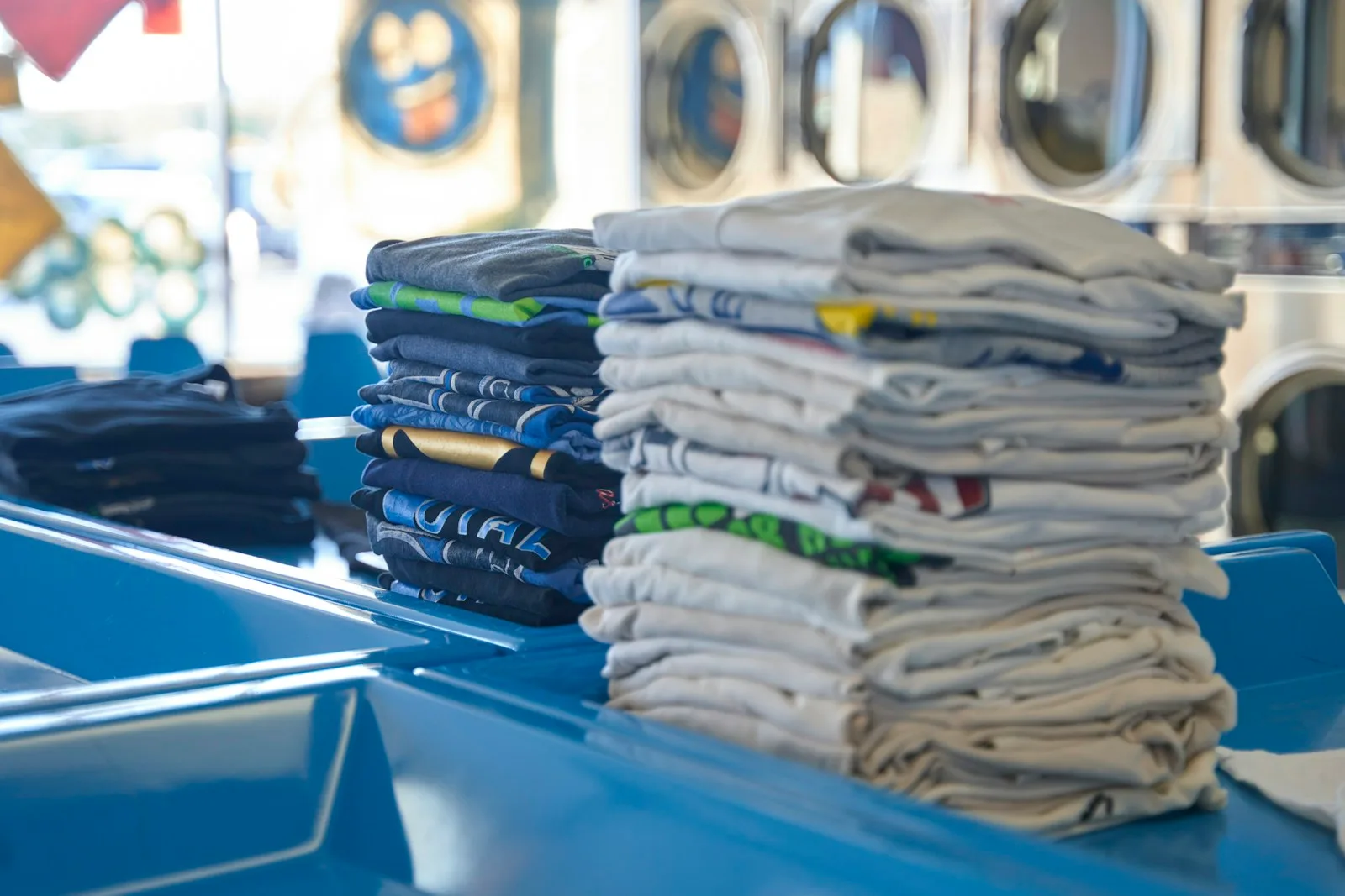 Folded everyday clothes on a work surface with washing machines in the background